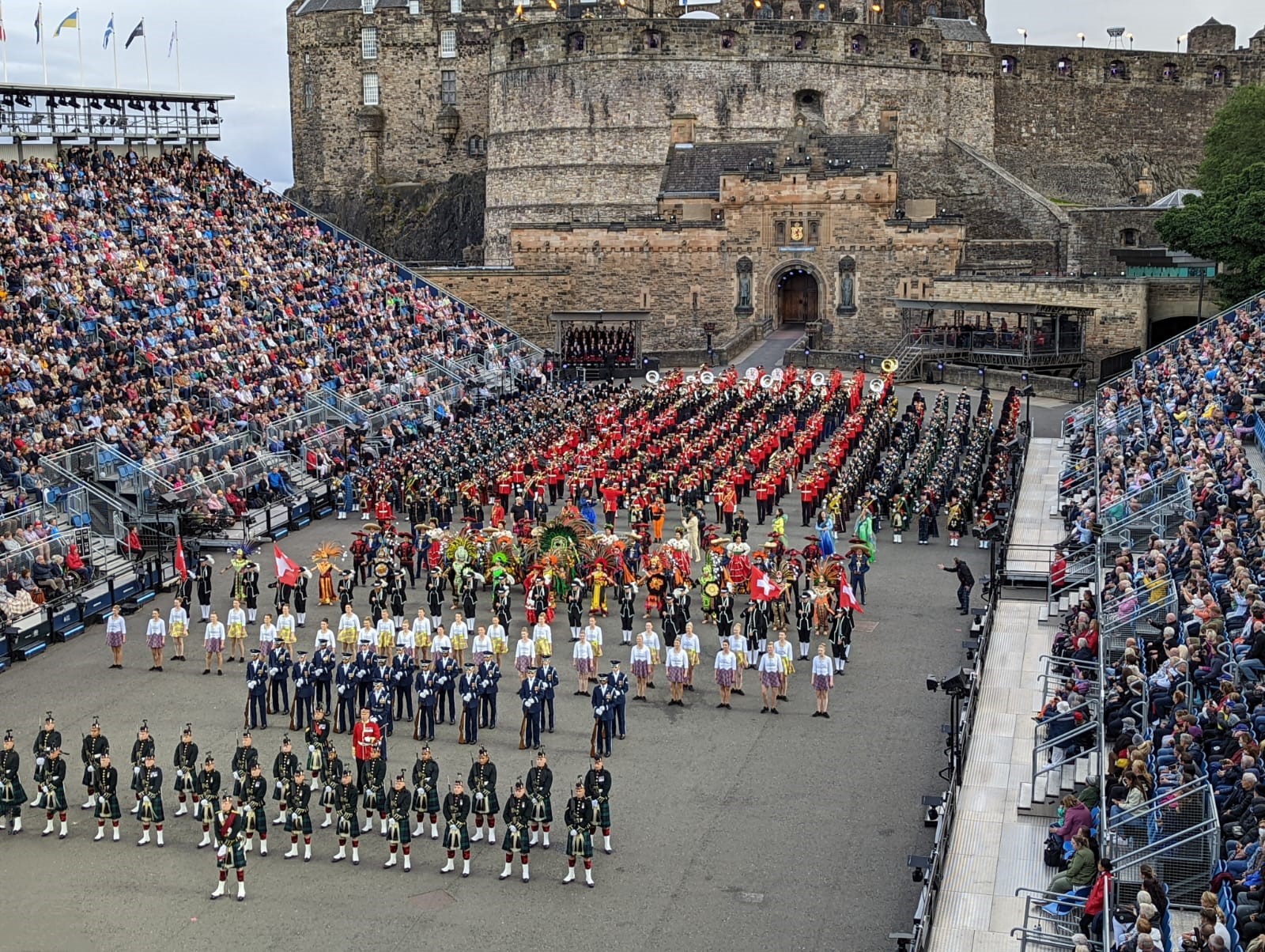 Image shows performers and musicians outside Edinburgh Castle, with crowds watching from the stands. 